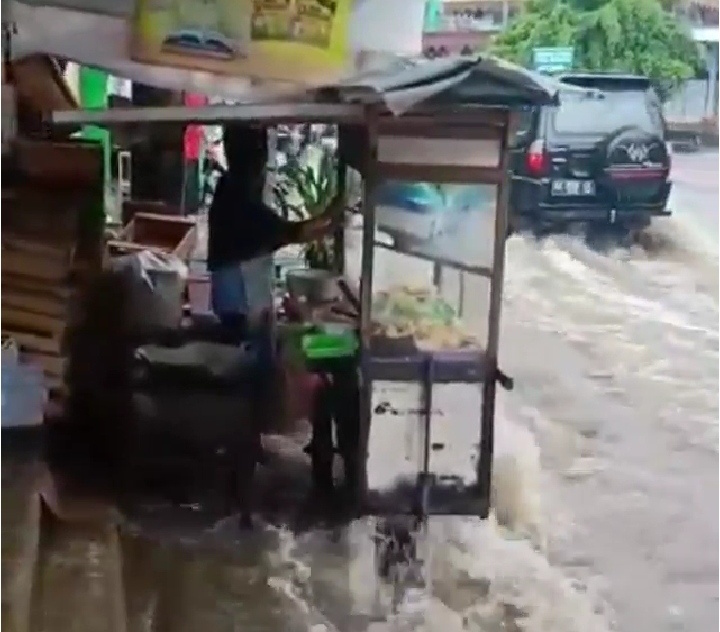 NEWS: Sebuah gerobag bakso dipegangi pemiliknya takut kebawa arus air yang melupa dari selokan memenuhi jalan blabak-sawangan (2/3/2020)-(Foto: Istimewa)