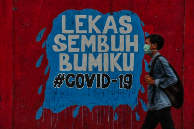 LEKAS SEMBUH: Seorang warga melintasi tembok mural yang berisi pesan agar bumi Indonesia segera sembuh dari covid-19. (Foto: Istimewa)