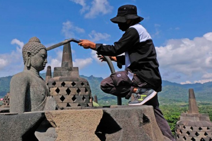 PANJAT: Petugas membersihkan patung dan stupa candi dari sisa debu vulkanik erupsi Gunung Merapi pekan lalu (21/6). (Foto: internet)