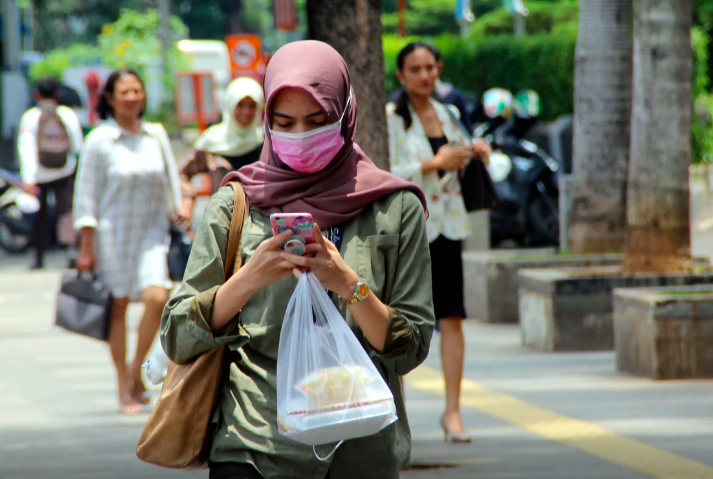 KONTRAS: Seorang perempuan bermasker ditempat umum dengan latar pejalan kaki tak memakai masker. (Foto: internet)