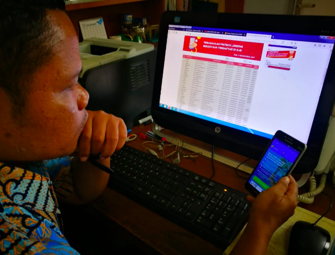 JELI: Seorang warga mencocokkan identitas penyedia layanan pinjaman online dengang daytar penyedia layanan berizin dari OJK, Selasa (14/7). (Foto: internet)
