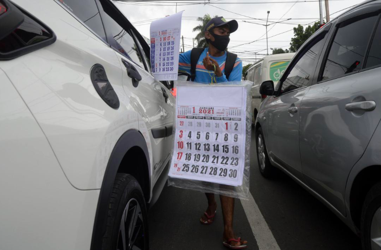 SELAMAT TAHUN BARU: Seorang penjual kalender 2021 menjajakan penanggalan di jalan. (foto: internet)