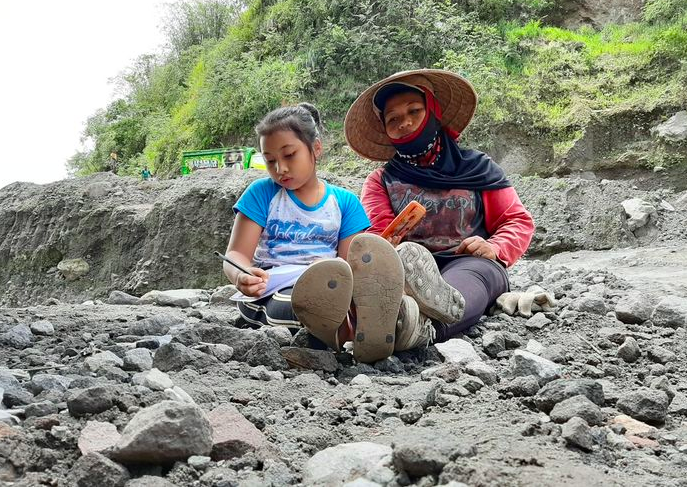 HEBAT: Seorang ibu meluangkan waktu menemani anaknya belajar disela kesibukan menambang pasir. (foto: ilustrasi)